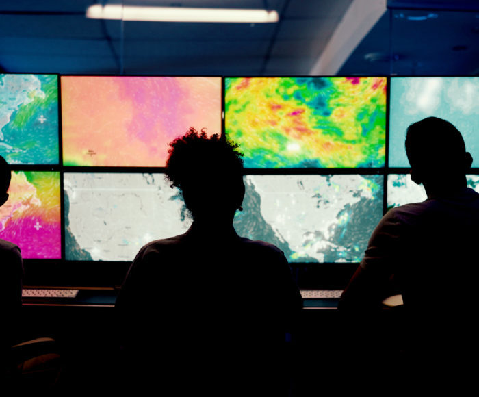 Weather, screen or monitor with people for forecast, satellite maps or teamwork to track storm. Control room, back or scientists with meteorology for broadcast news, report or silhouette at night